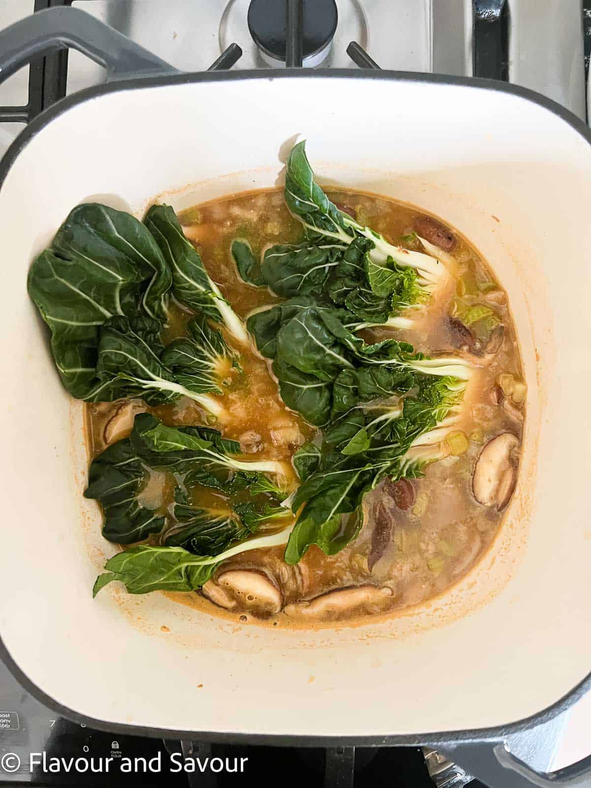 Adding baby bok choy to a soup pot of miso noodle soup.