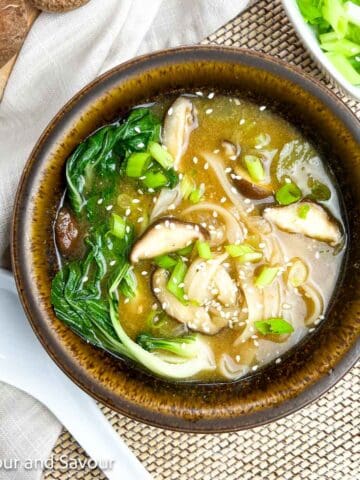 Miso noodle soup with baby bok choy, shiitake mushrooms, oyster mushrooms, garnished with green onions and sesame seeds.