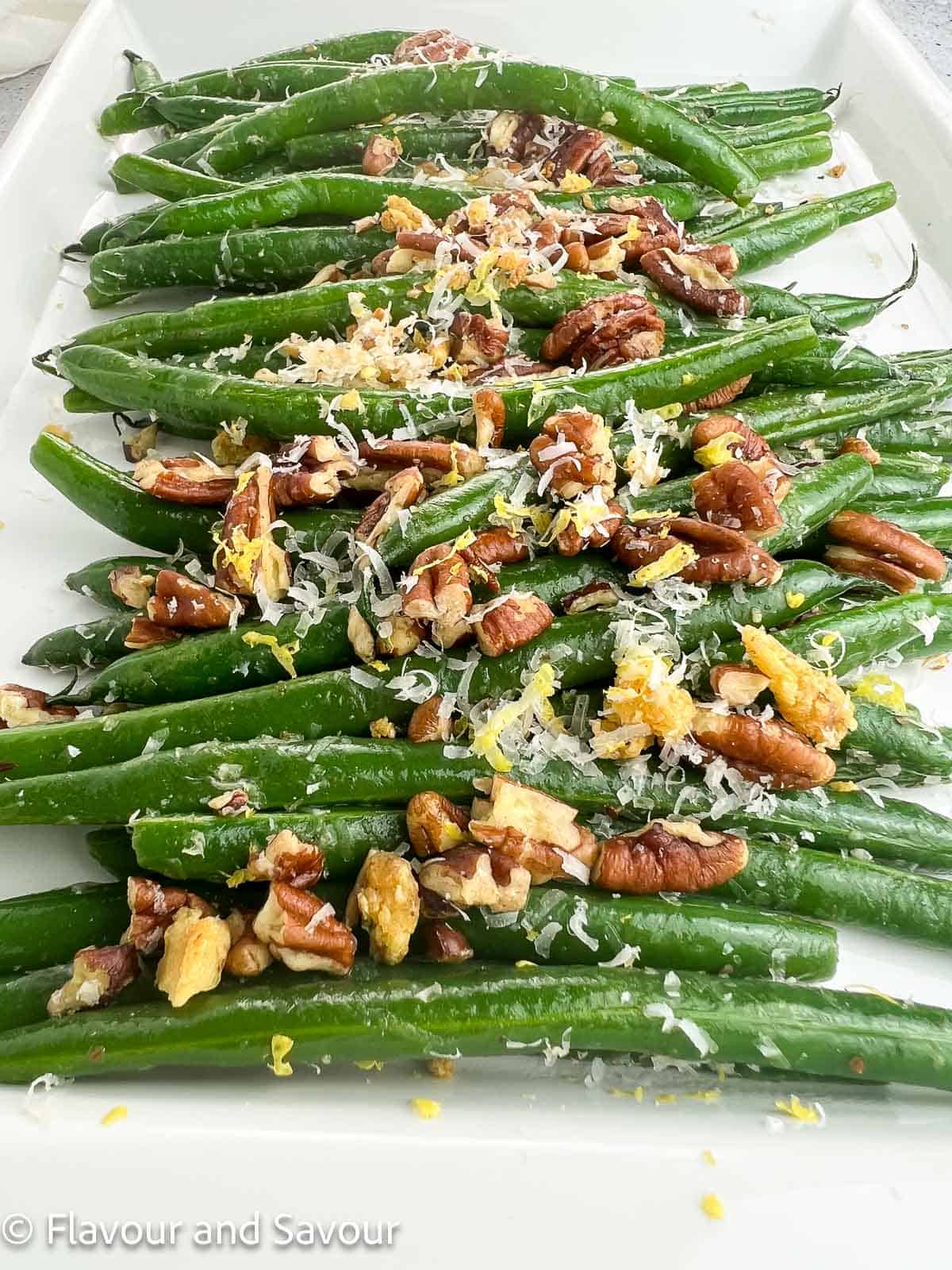 Close up view of sauteed green beans on a serving plate topped with pecans and parmesan cheese.