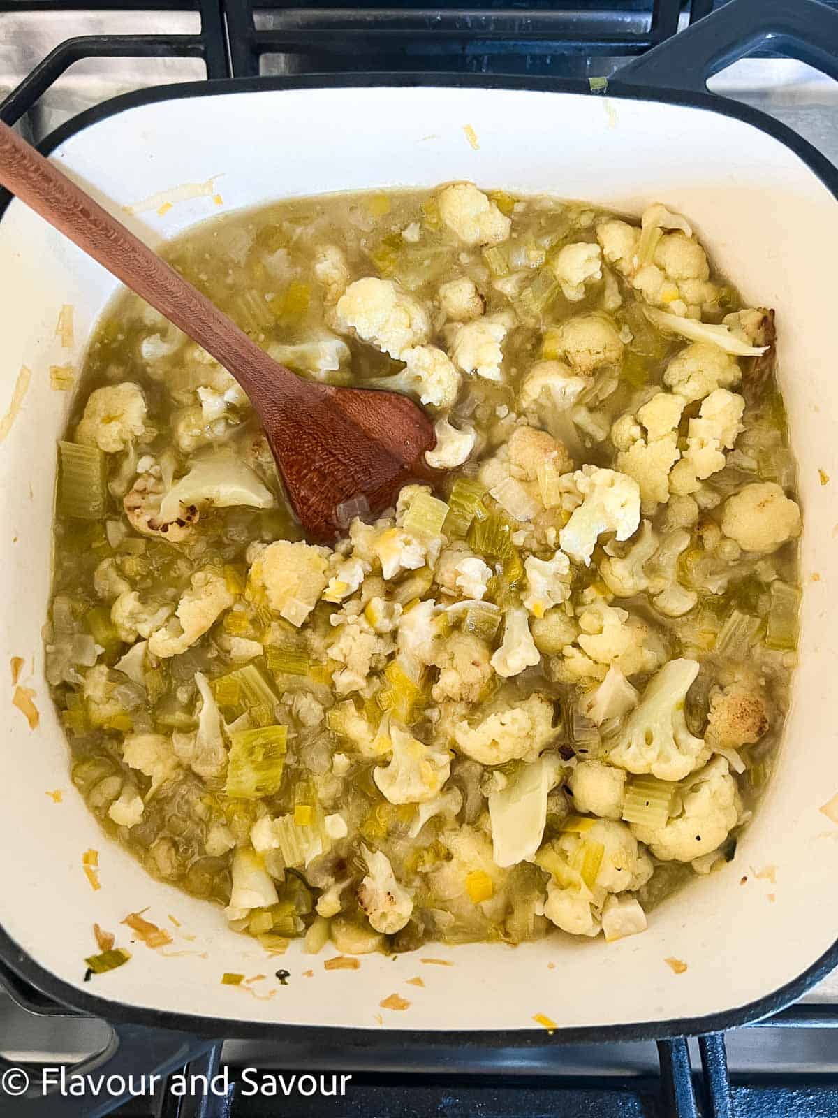 Sautéed vegetables, roasted cauliflower florets and broth in a soup pot for cauliflower soup.