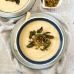 A bowl of roasted cauliflower soup with a small dish of pumpkin seeds beside it.