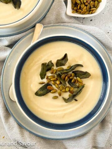 A bowl of roasted cauliflower soup with a small dish of pumpkin seeds beside it.