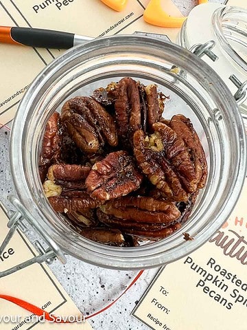 Overhead view of a small jar of roasted pumpkin spice pecans with printable gift tags beside it.