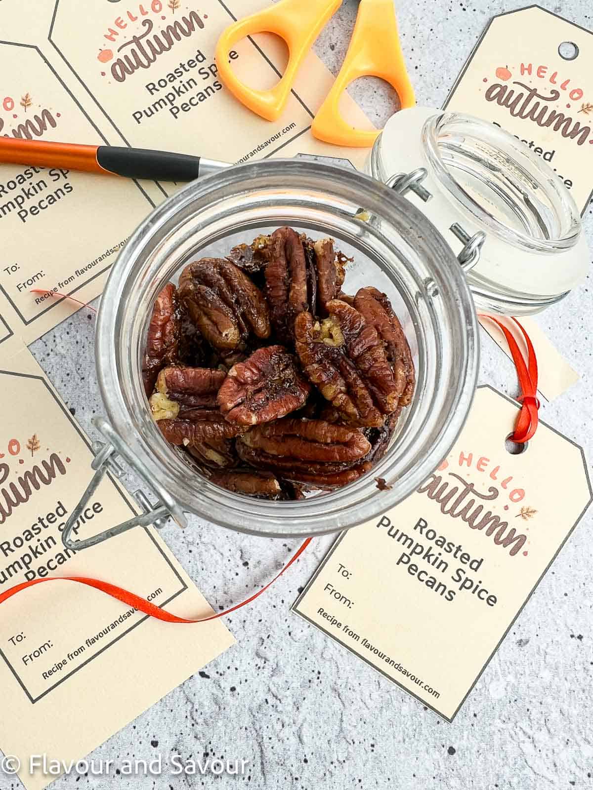 Roasted pumpkin spice pecans in a jar with gift tags beside it.
