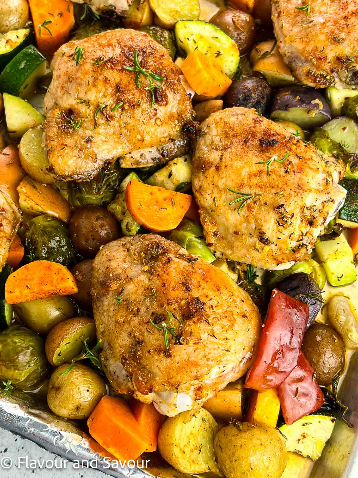 Closeup overhead view of chicken and roasted vegetables on a sheet pan.