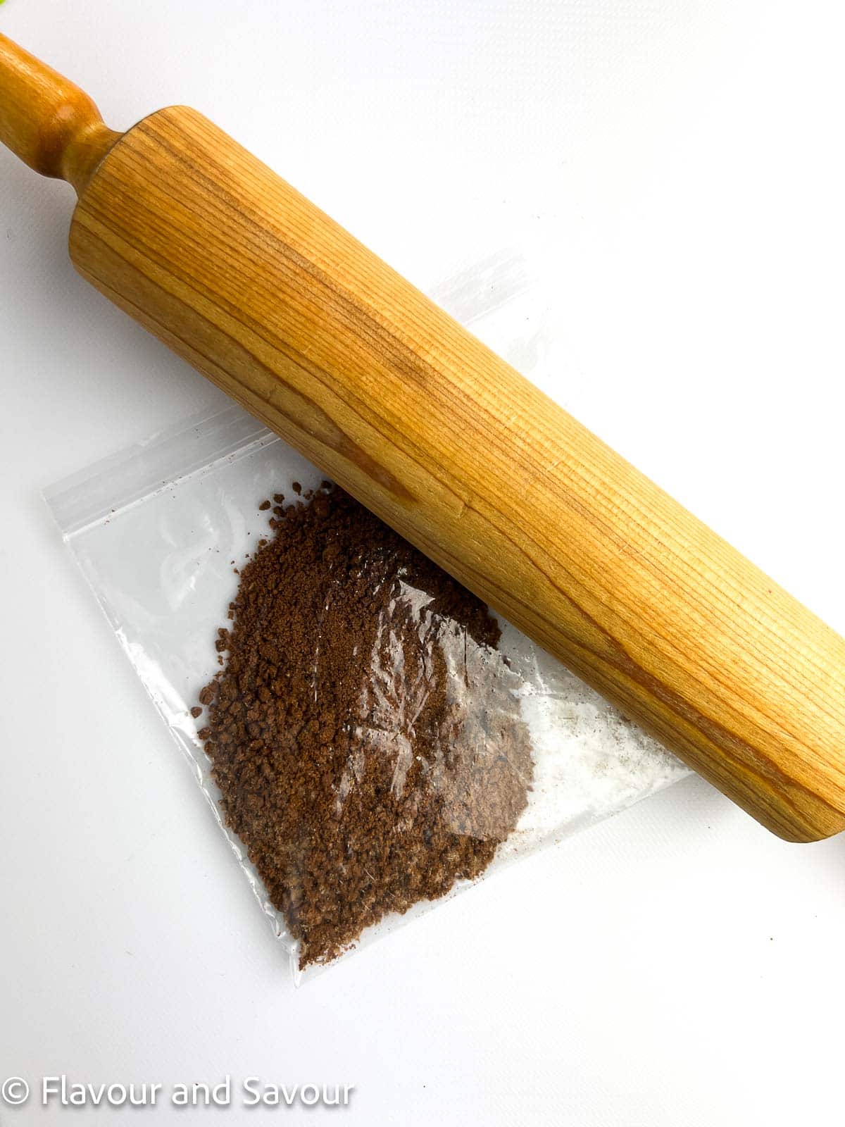 A rolling pin and a bag of chocolate cookie crumbs, showing how to crush cookies in a resealable bag.