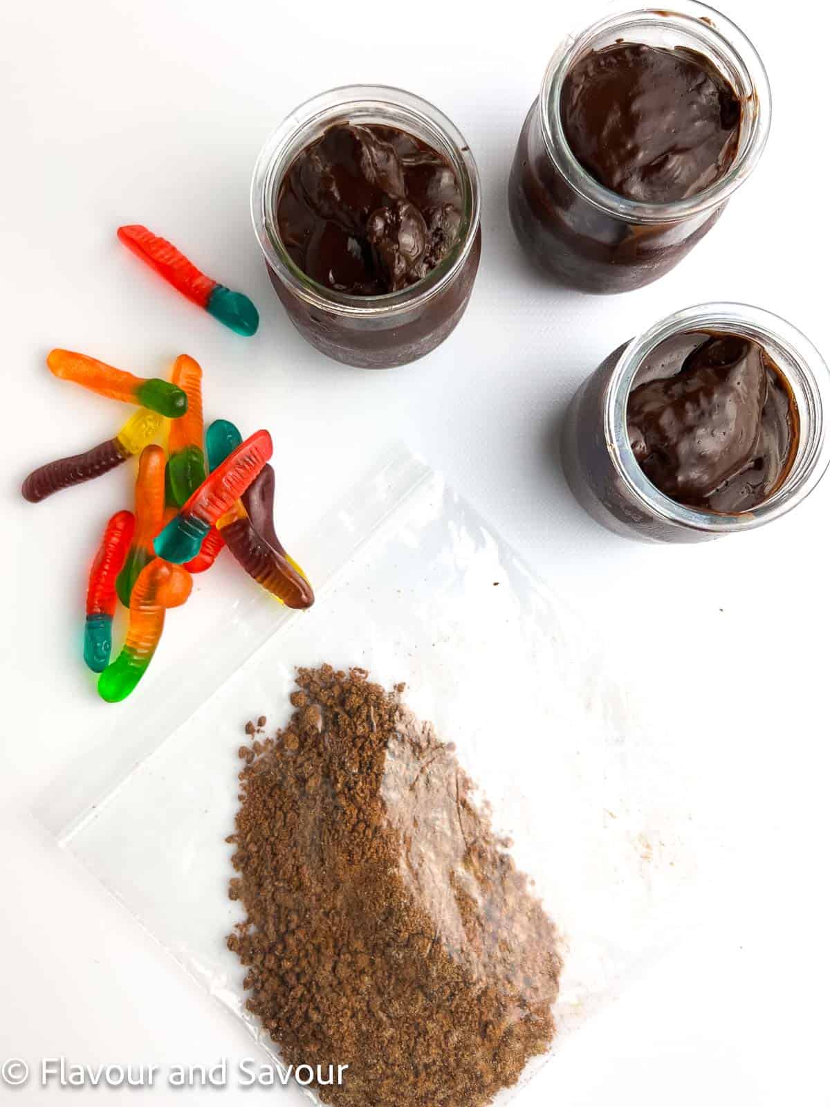 Ingredients for dirt and worms pudding cups: chocolate pudding, gummy worms, and crushed chocolate cookie crumbs.