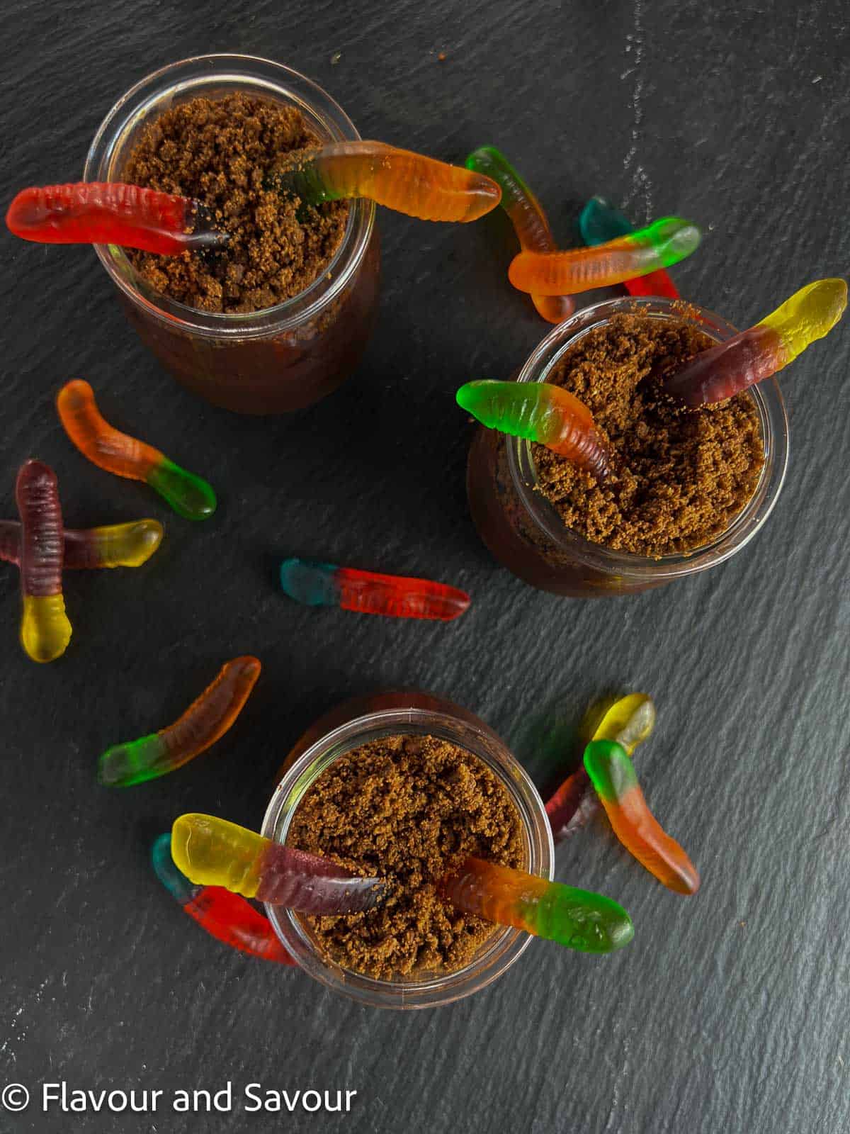 Dirt and worms pudding cups on a black slate serving board.