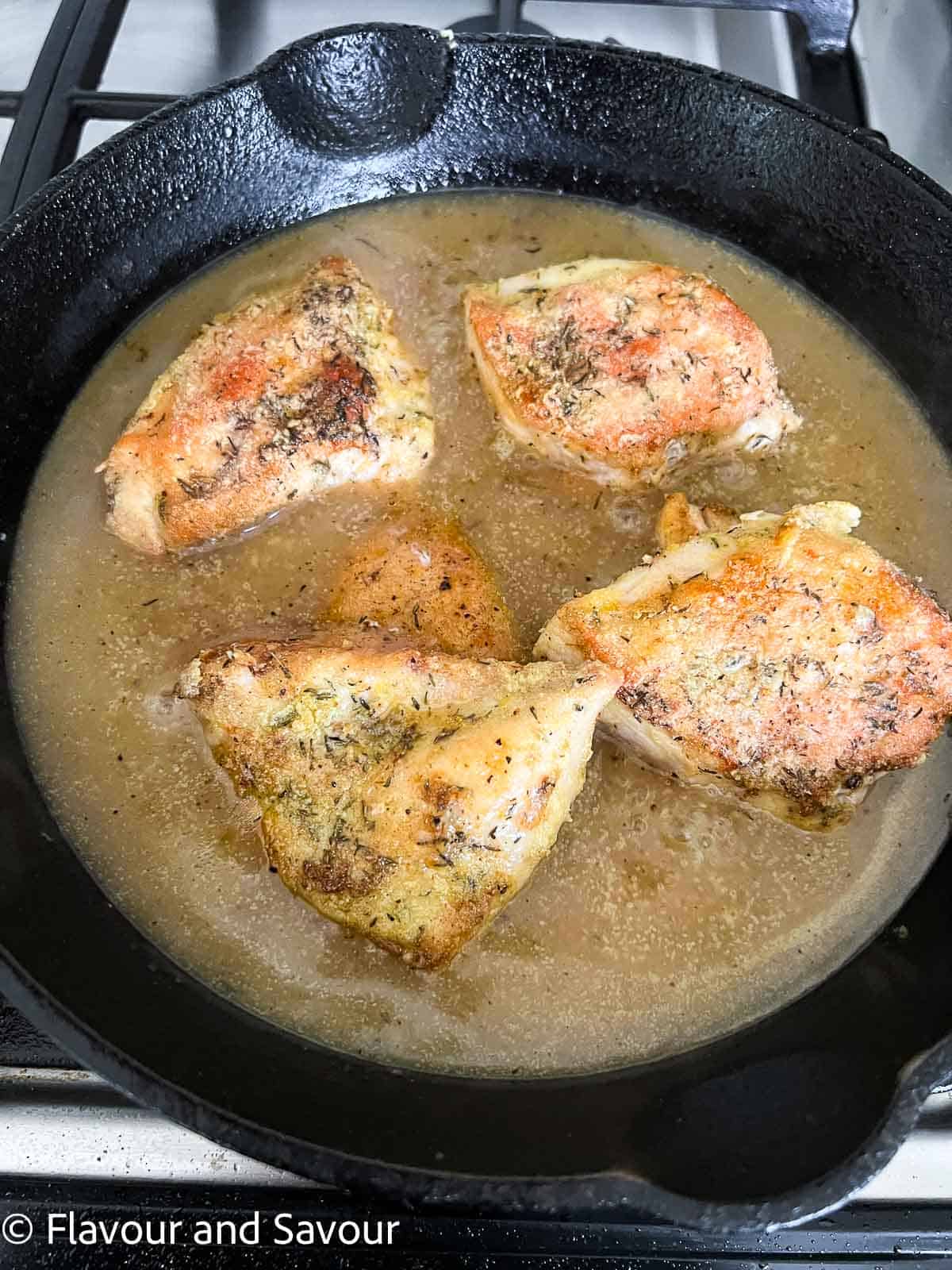 Browned chicken breasts in sauce in a cast iron pan.