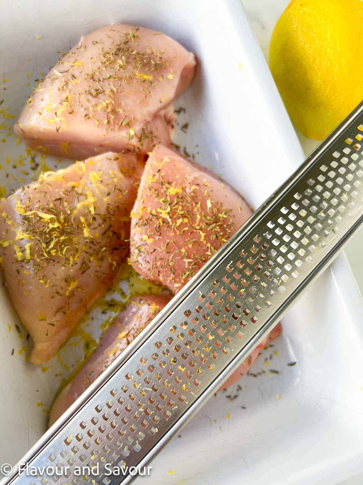 Raw chicken breasts coated with salt, pepper and lemon zest.