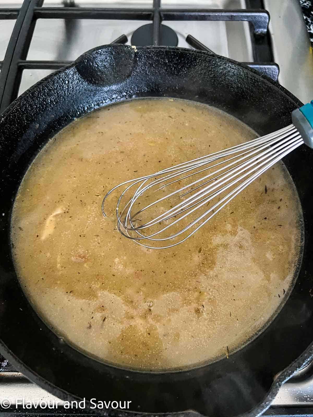 Sauce for chicken with prosciutto in a cast iron skillet with a whisk.