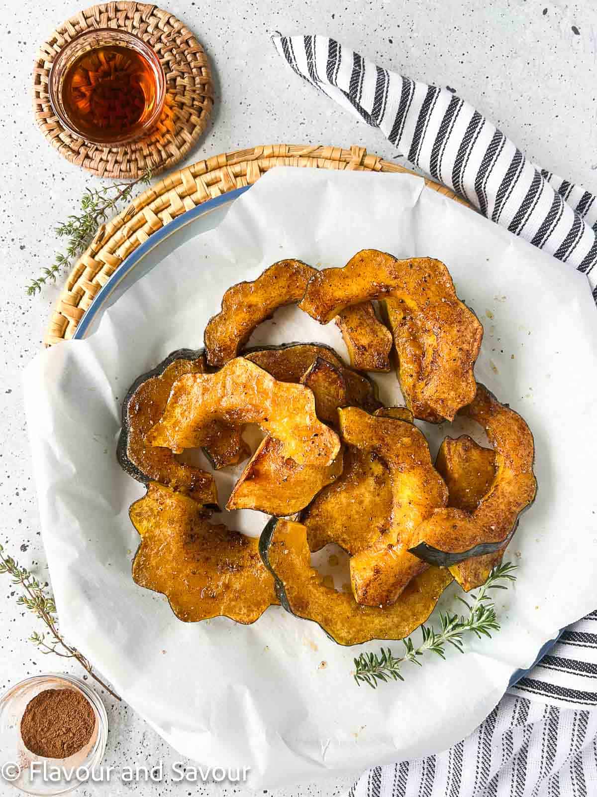 A platter of acorn squash slices cooked in an air fryer with small bowls of maple syrup and cinnamon nearby.