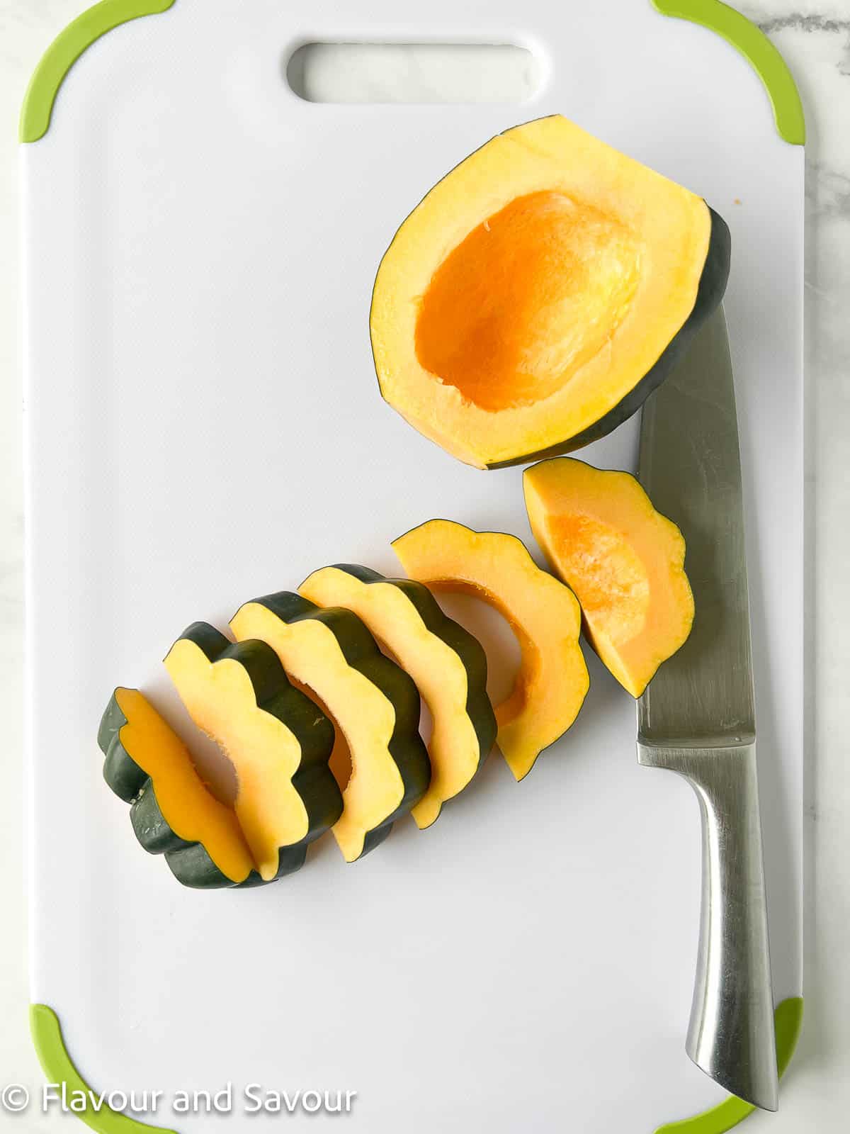 An acorn squash cut into ¾ inch thick slices on a cutting board with a chef's knife beside.