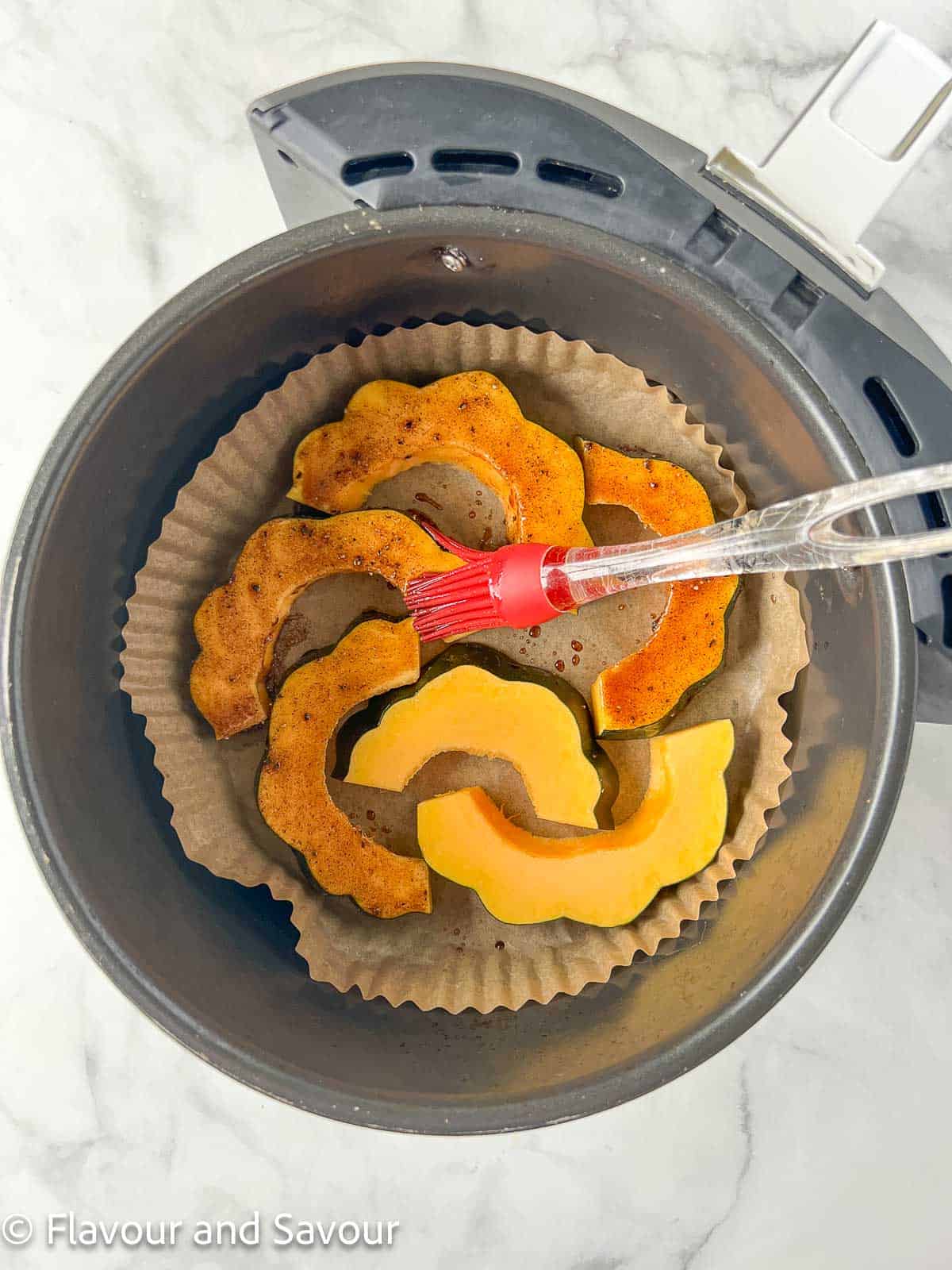 Acorn squash slices in an air fryer basket brushed with a mixture of olive oil, cinnamon, salt and pepper.