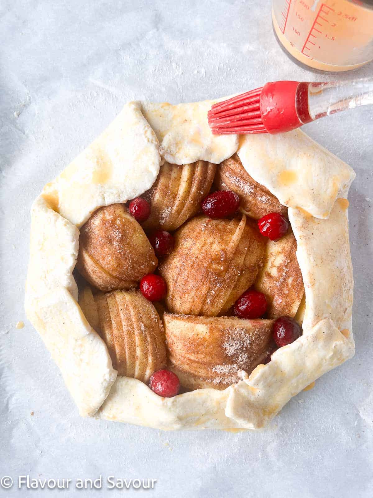 Brushing beaten egg on pastry edges of apple cranberry galette.