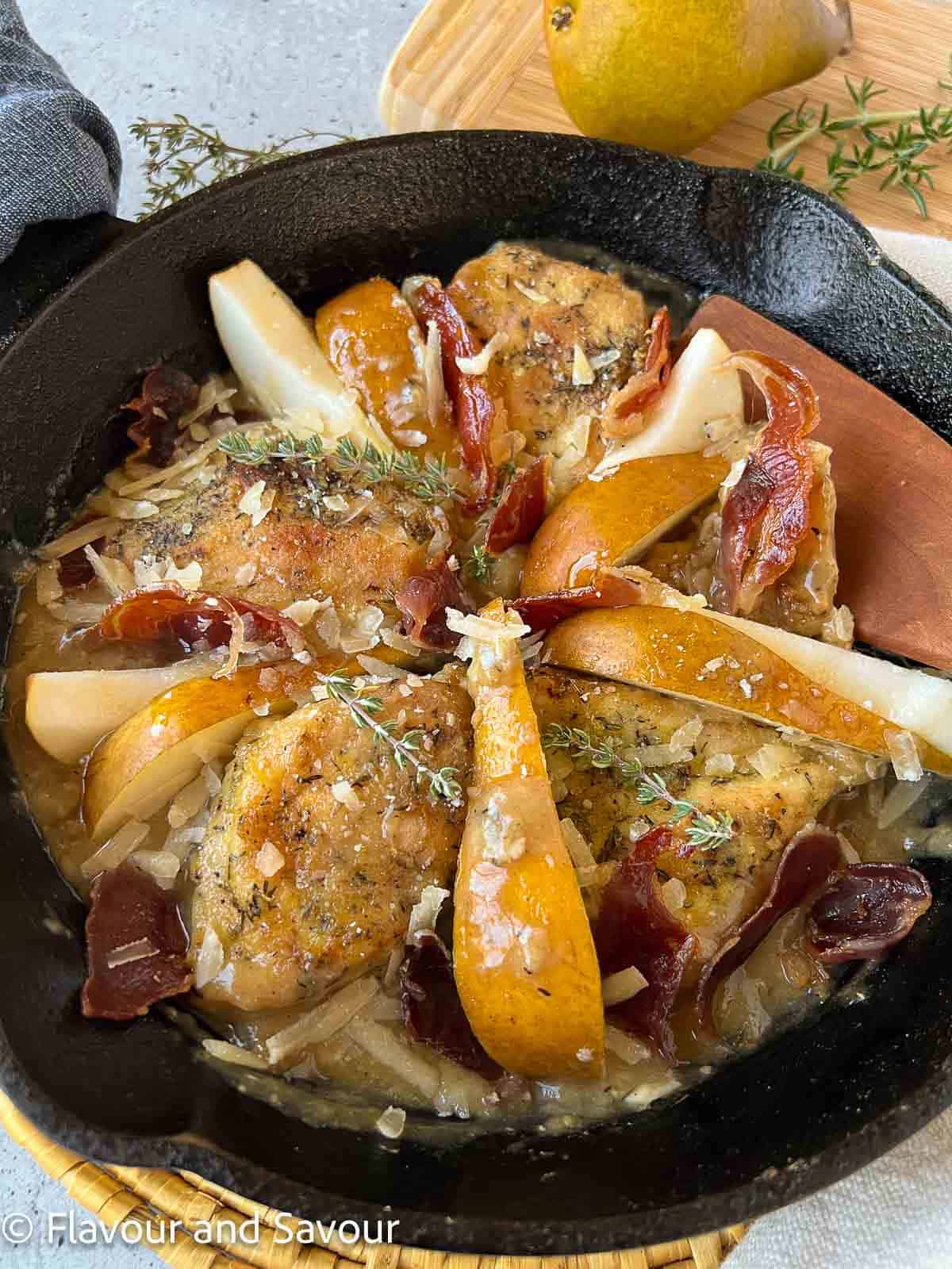A cast iron pan with baked chicken breasts, sliced pears and small pieces of prosciutto.
