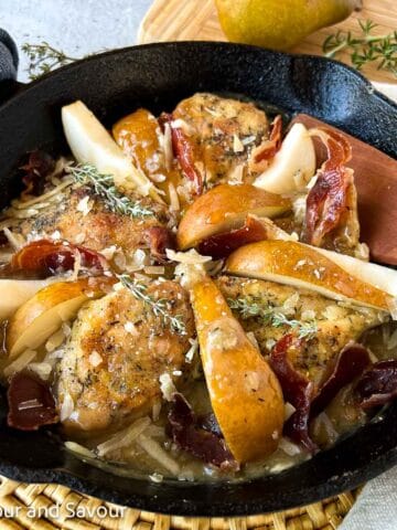 Square image of one-pan chicken with prosciutto, pears and parmesan cheese in a cast iron skillet.