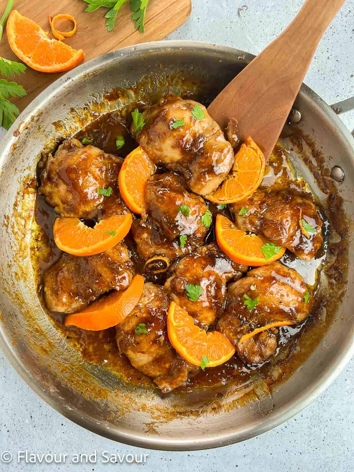 Hoisin orange chicken thighs in a skillet with orange slices, garnished with parsley.