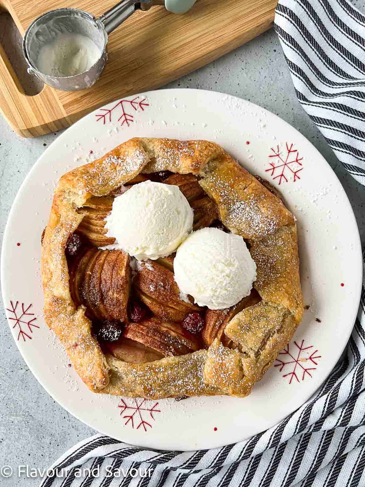 Puff pastry apple cranberry galette with two scoops of ice cream on a serving plate.