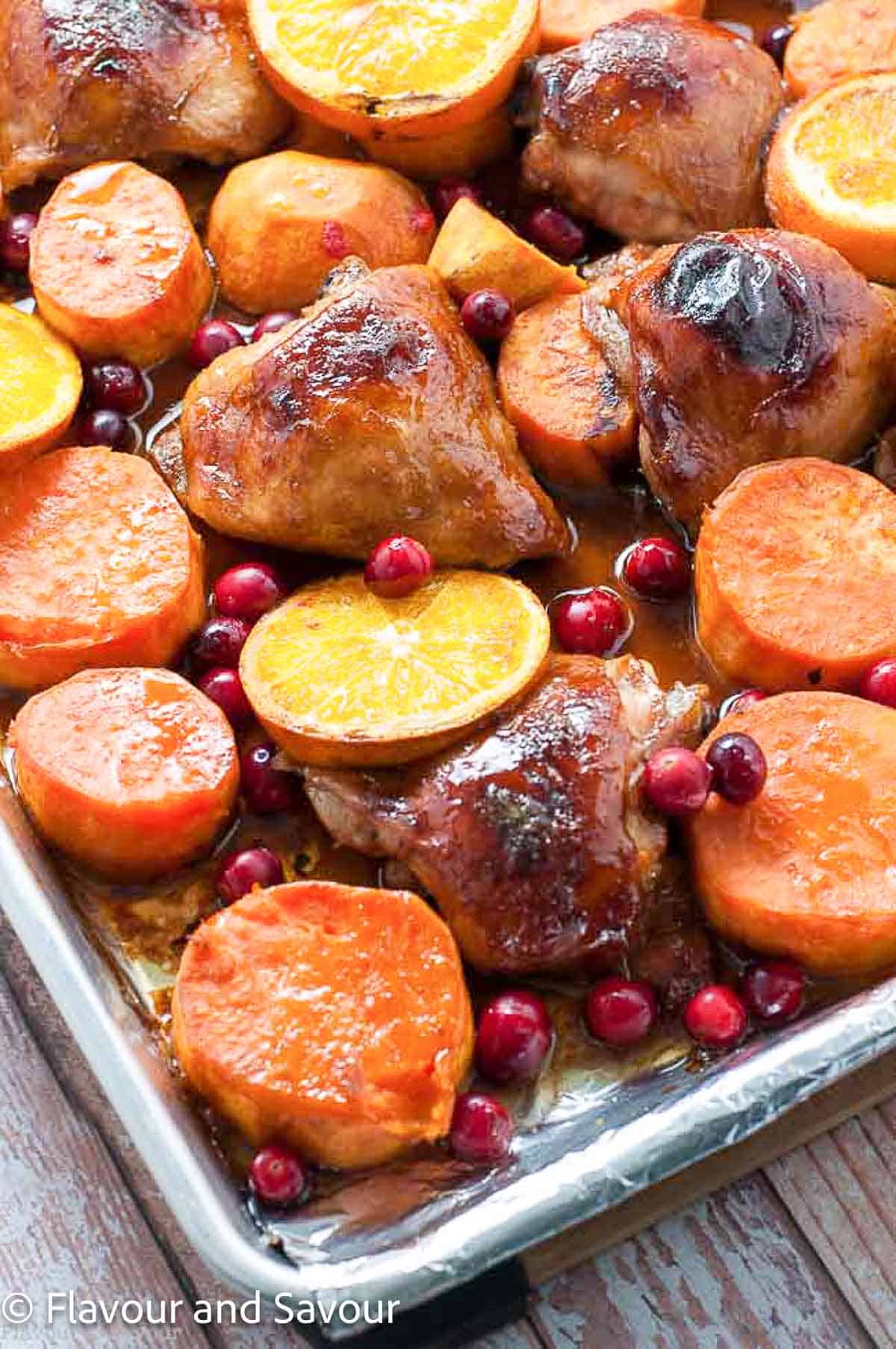 Chicken thighs with hoisin sauce, sweet potatoes, sliced oranges and fresh cranberries baked on a sheet pan.
