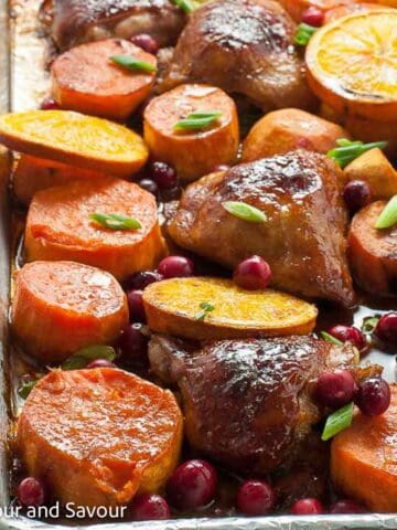 Square image of a sheet pan dinner of hoisin chicken thighs, sweet potatoes, orange slices, and cranberries.