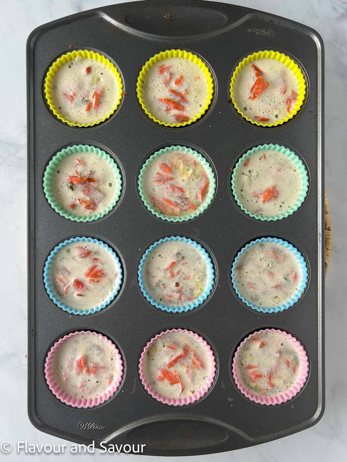 Egg mixture added to mini smoked salmon quiche in silicone cups.