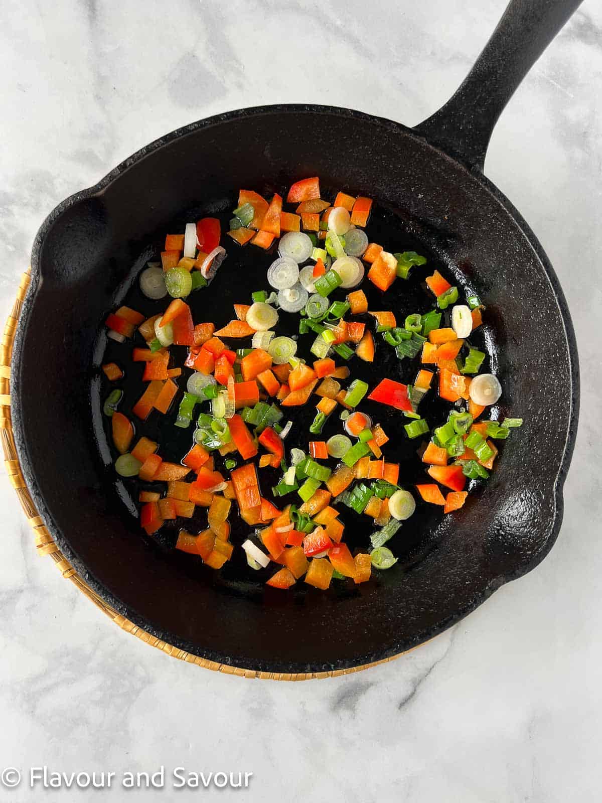 Chopped red bell pepper and green onions in a cast iron skillet.