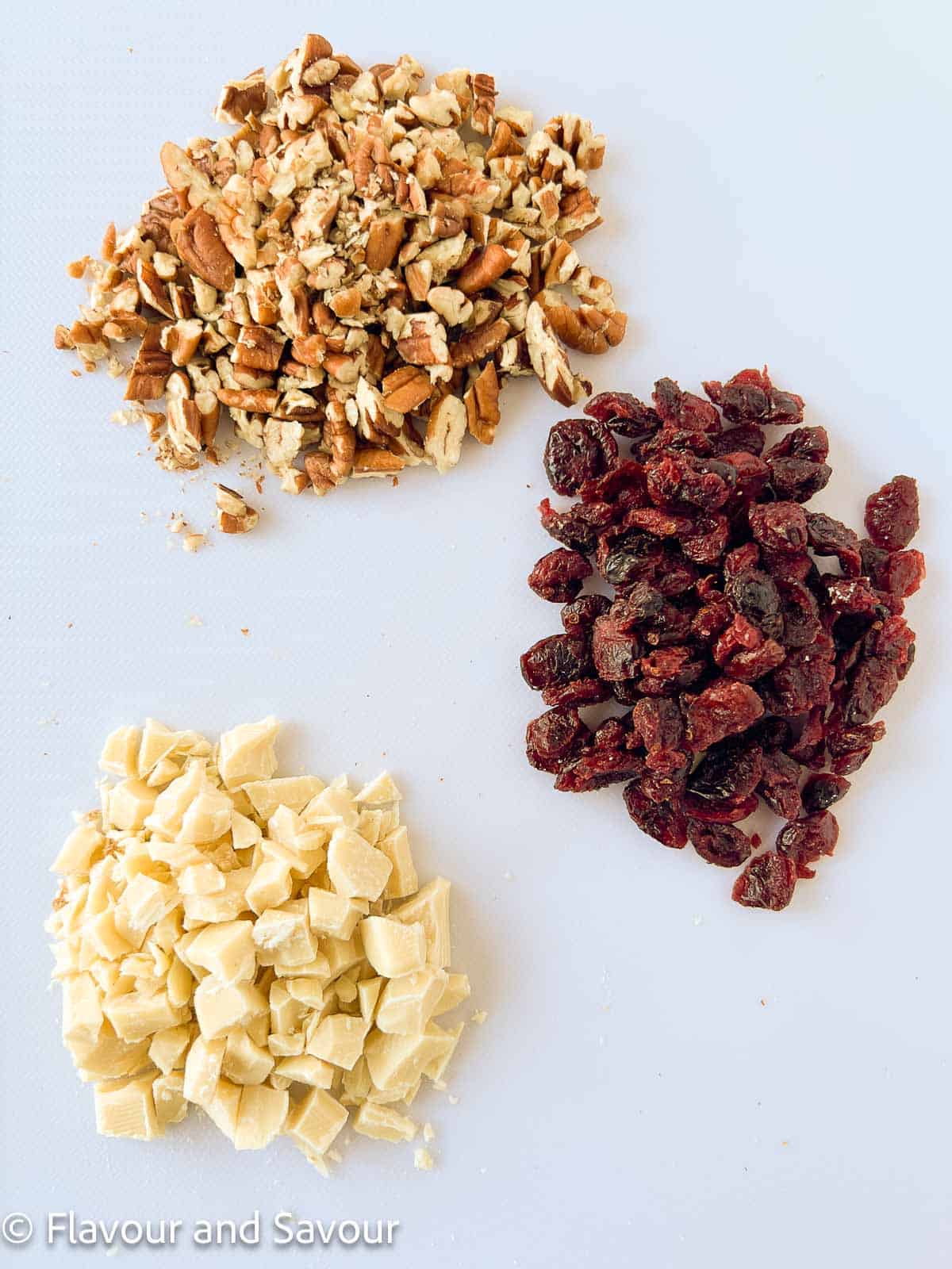 Chopped pecans, dried cranberries and white chocolate in small piles.
