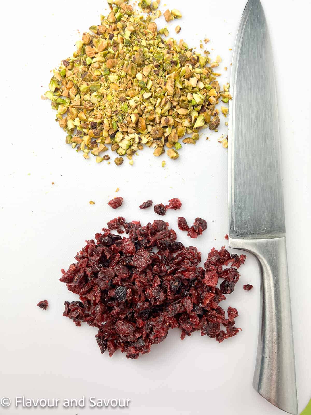 Chopped pistachios and chopped dried cranberries on a cutting board with a knife.