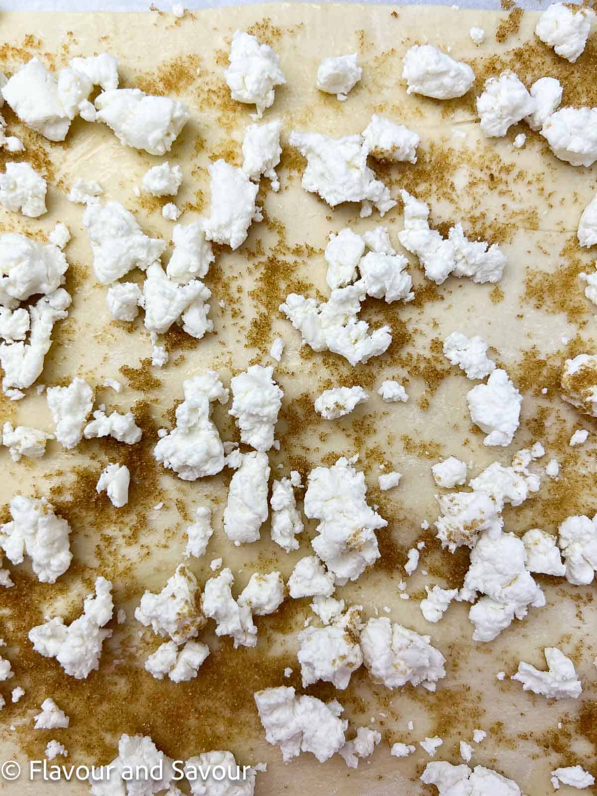 A sheet of puff pastry topped with brown sugar and crumbled goat cheese.