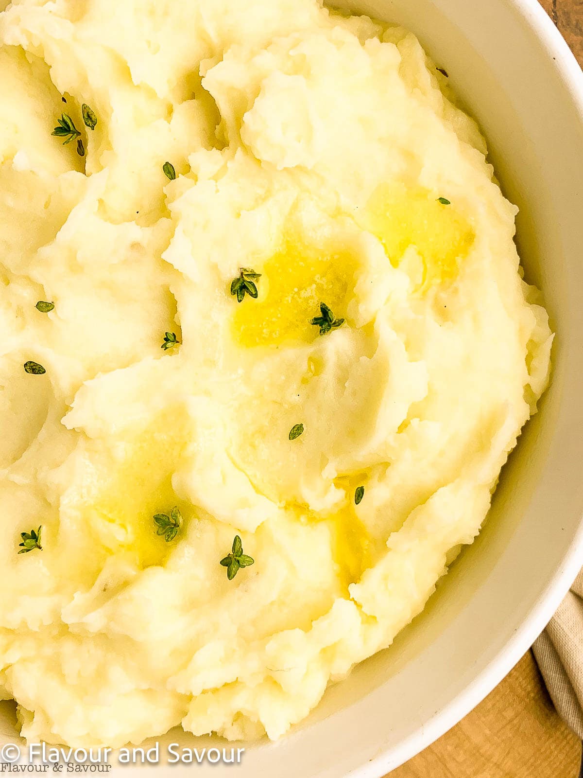 A bowl of mashed potatoes with butter and fresh thyme leaves.