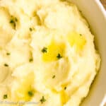 A bowl of mashed potatoes with melted butter and fresh thyme.