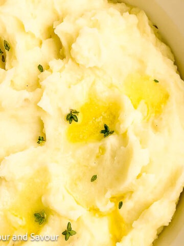 A bowl of mashed potatoes with melted butter and fresh thyme.