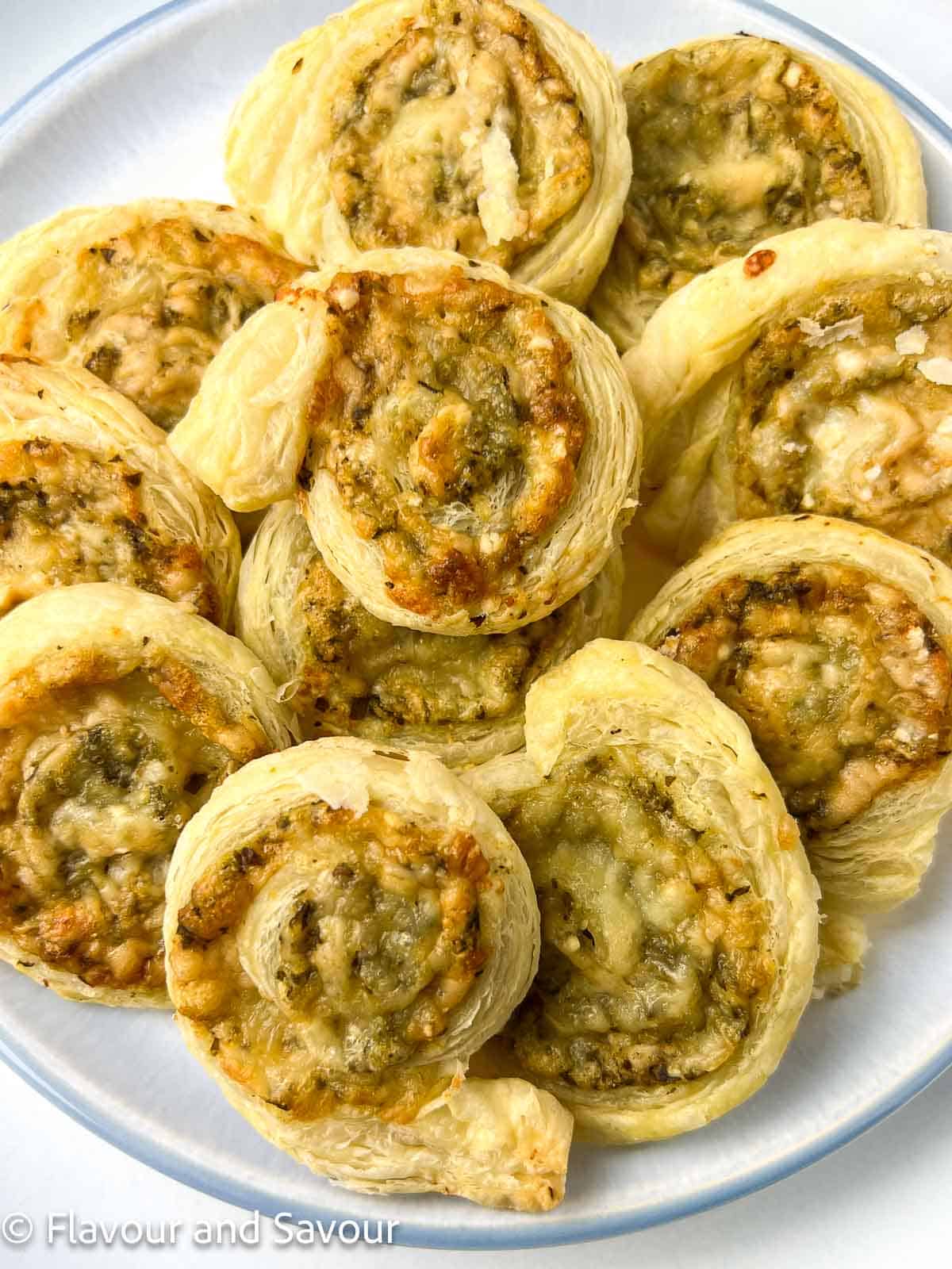 Puff pastry pesto pinwheels arranged overlapping on a plate.