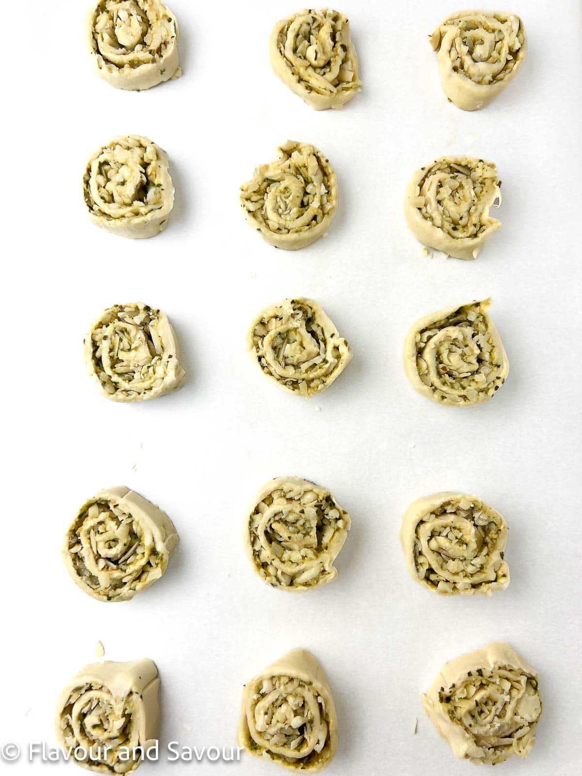 Slices of puff pastry pesto pinwheels arranged 2 inches apart on a baking sheet.