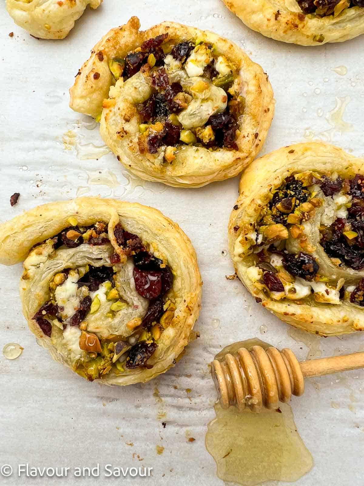 Three cranberry pistachio puff pastry pinwheels on a baking sheet drizzled with honey.