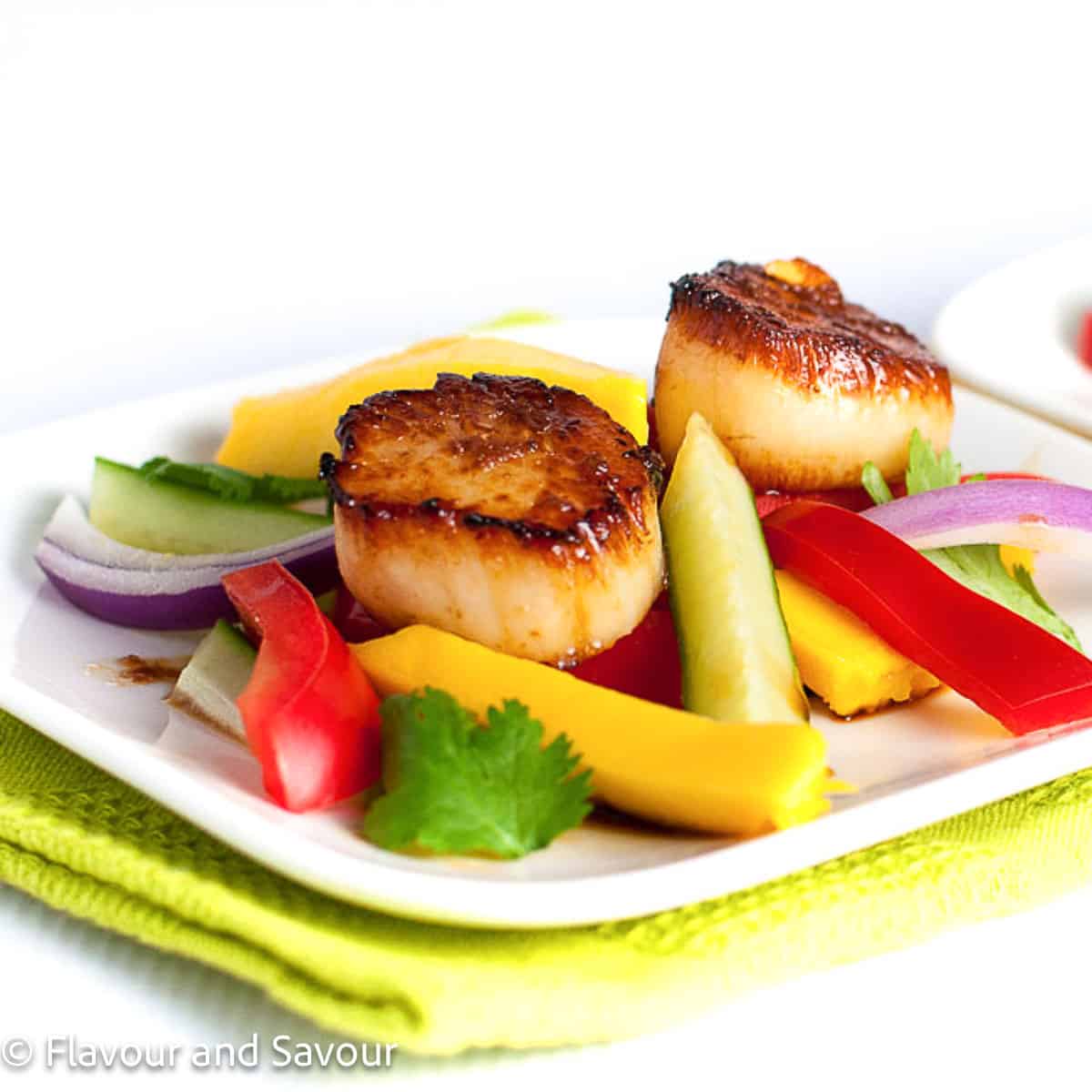 Two seared scallops with fresh sliced vegetables.