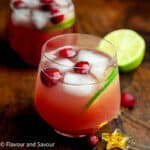 A glass of sparkling cranberry pineapple punch garnished with fresh cranberries and a slice of lime.