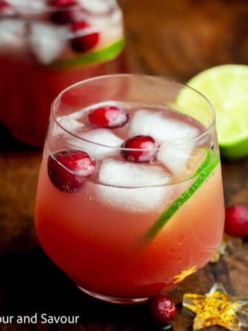 A glass of sparkling cranberry pineapple punch garnished with fresh cranberries and a slice of lime.