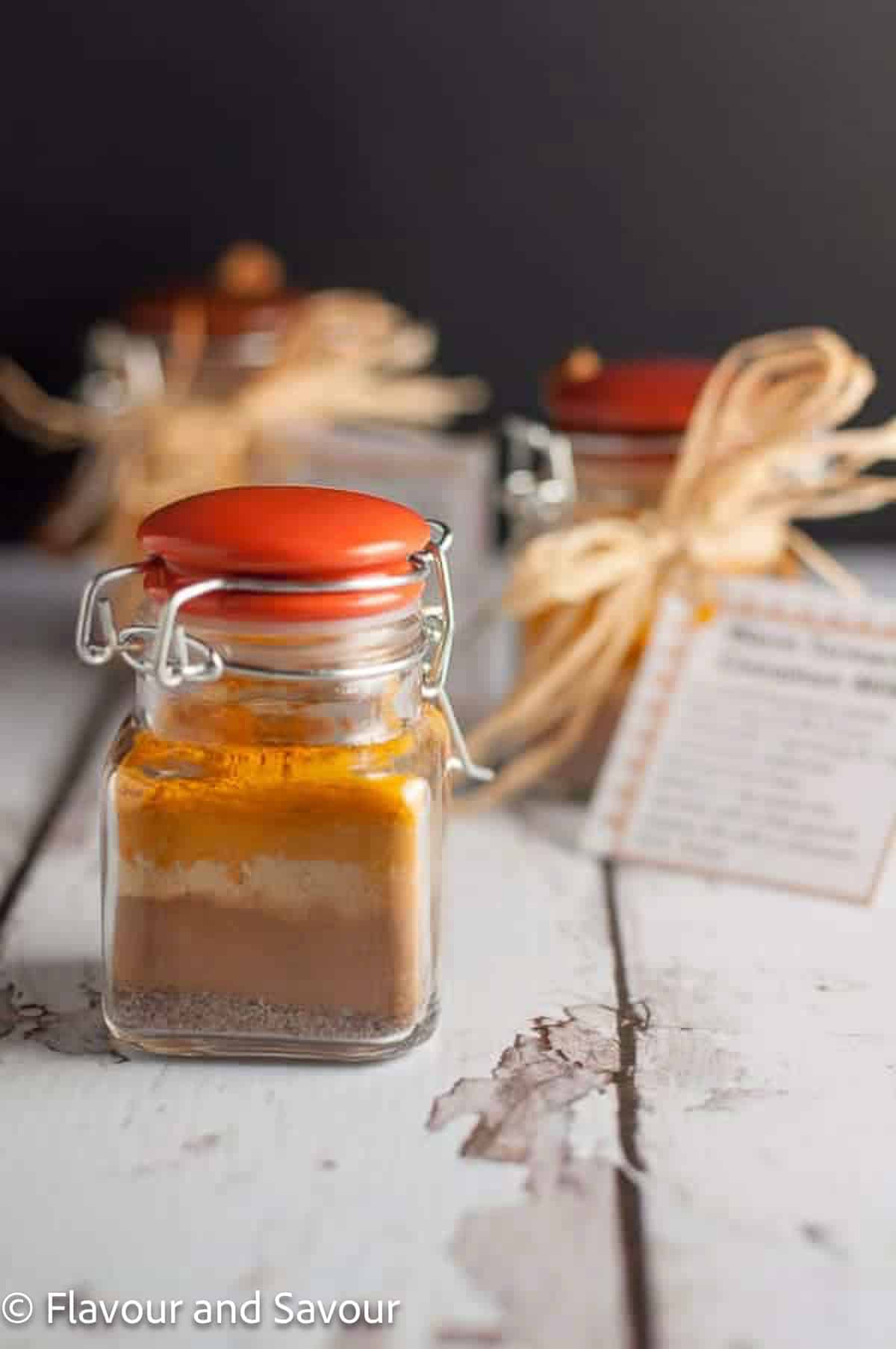Tiny jars of warm turmeric cinnamon milk spice mix with gift tags, tied with raffia.