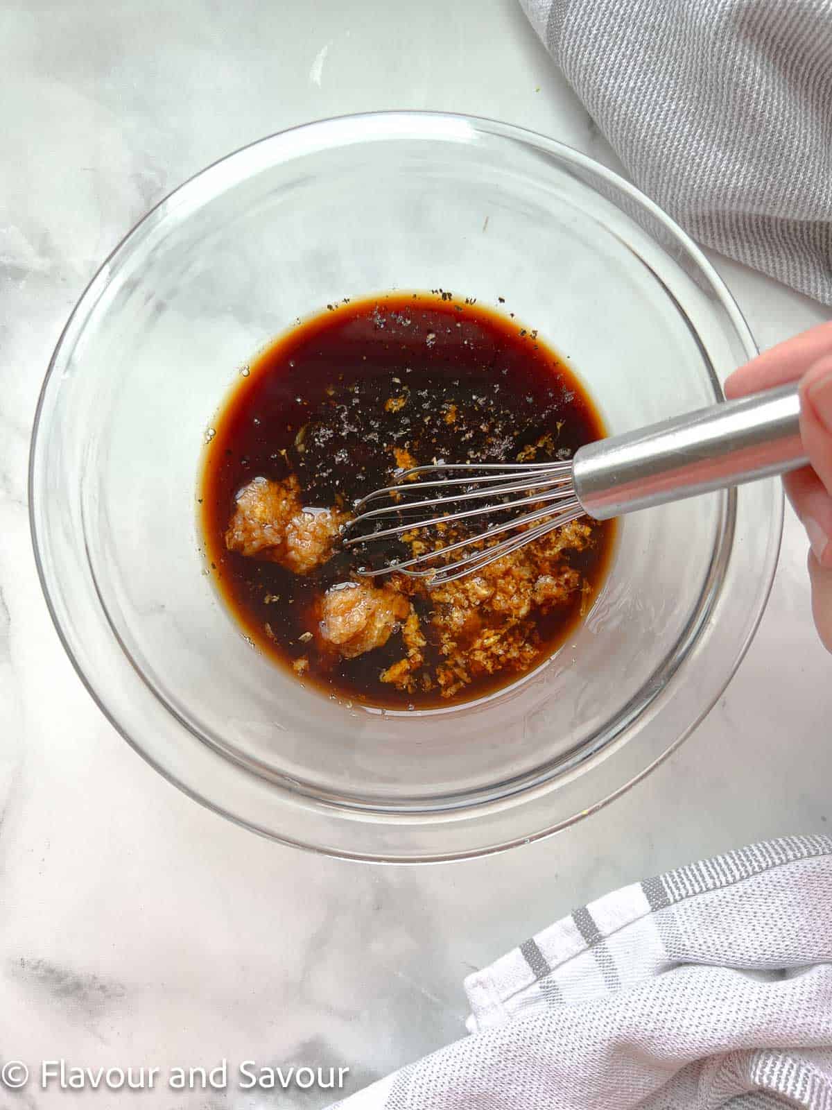 A bowl with ingredients for maple garlic marinade with a whisk.