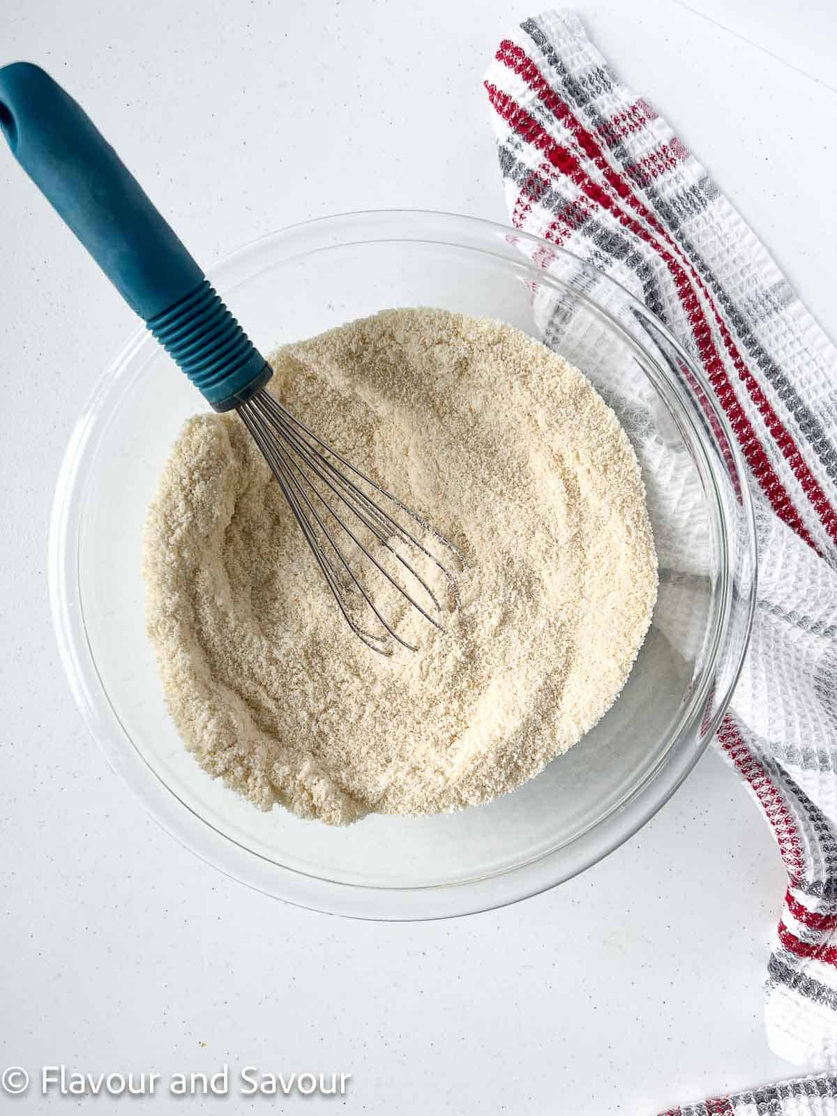 Almond flour, sugar and salt in a bowl with a whisk for amaretti cookies.