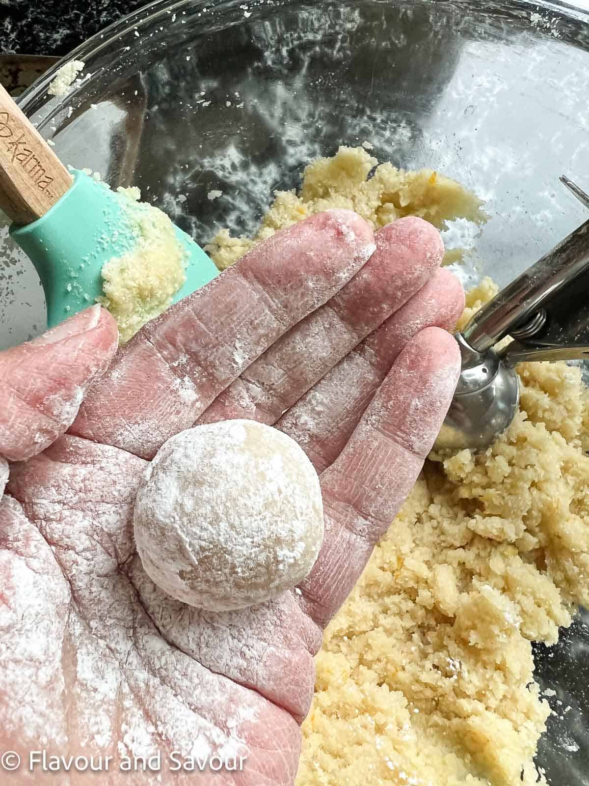 Rolling amaretti cookie dough ball with confectioner's sugar in the palm of a hand.