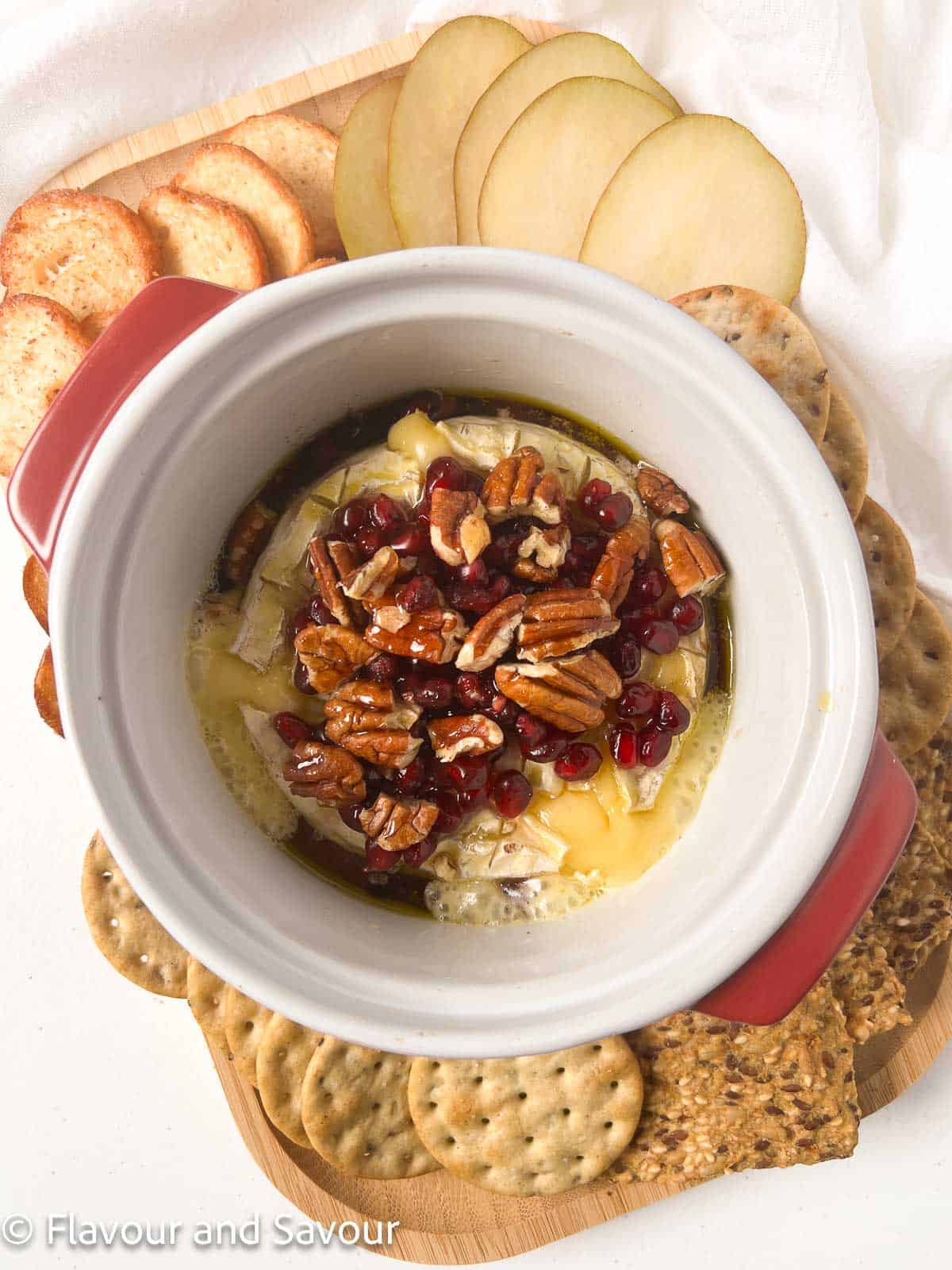 Baked Brie cheese in a baking dish surrounded by crackers and sliced pears.