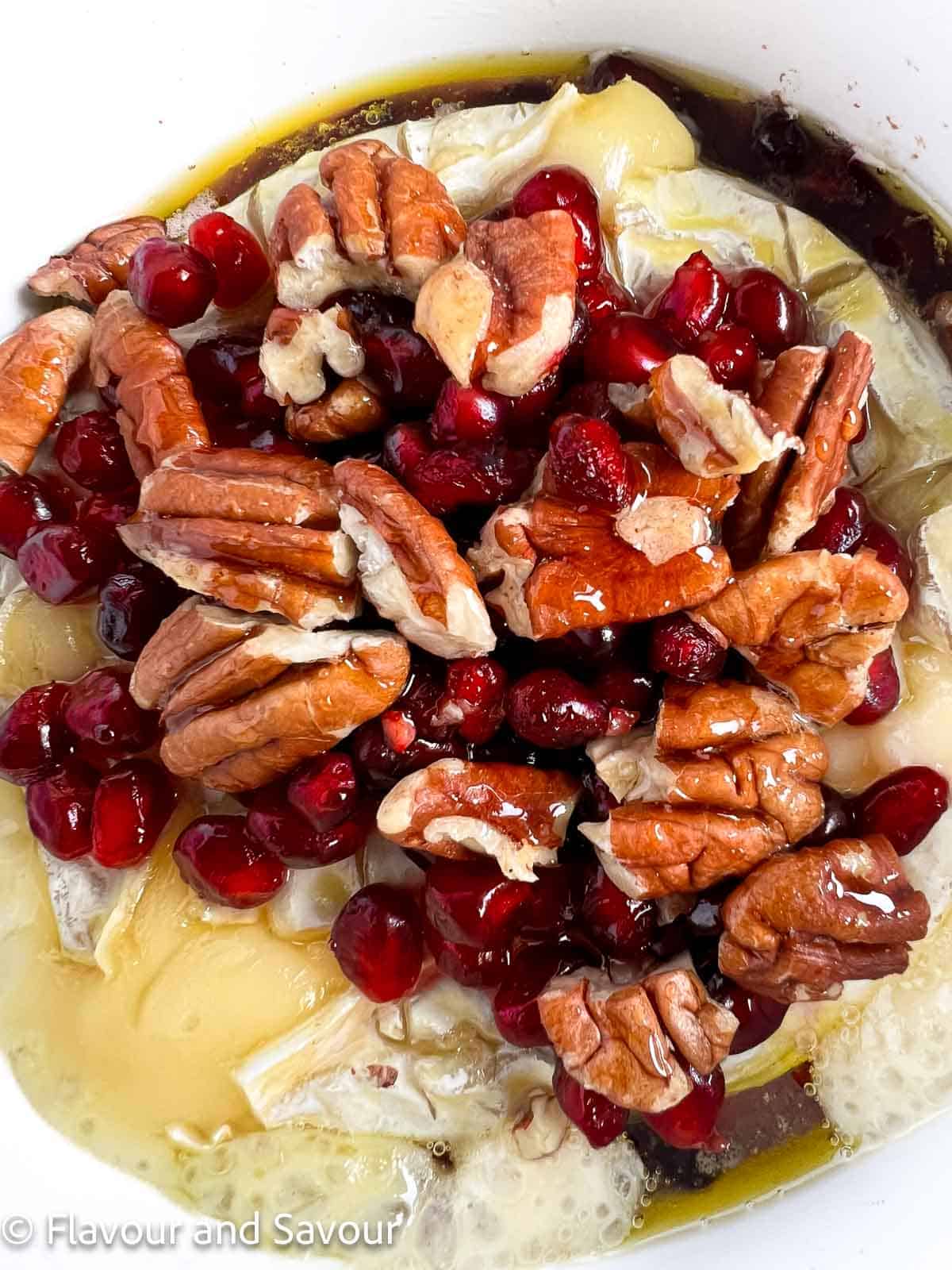 A wheel of baked Brie cheese topped with pomegranates, pecans and hot honey.