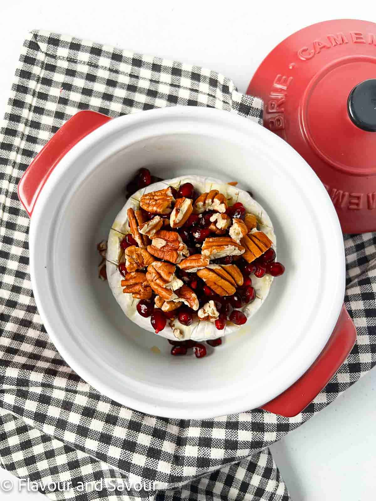 A round of baked Brie with pecans and honey in a Brie baking dish.