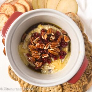 Square image of baked Brie cheese in a baking dish surrounded by crackers and sliced pears.