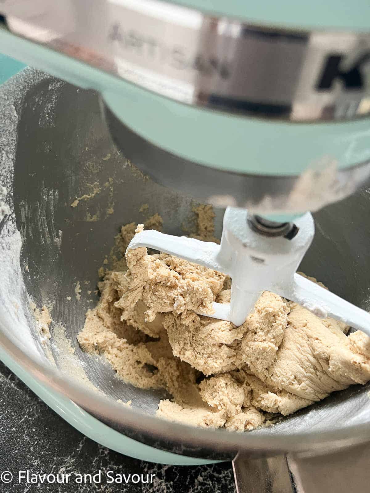 Dry ingredients added to toffee chocolate chip cookie batter in the bowl of a stand mixer.