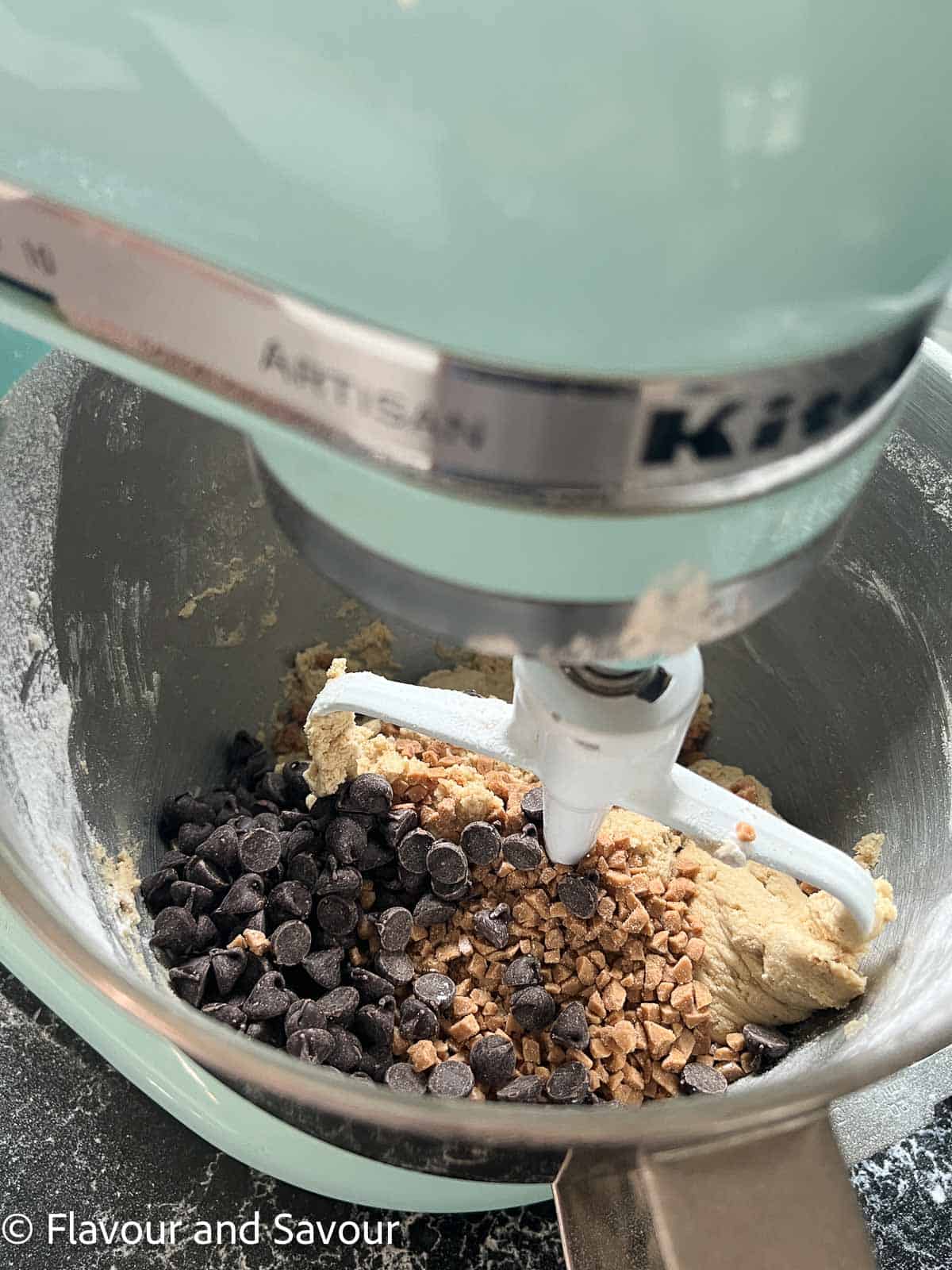 Toffee chocolate chip cookie batter in a bowl with chocolate chips and toffee bits.