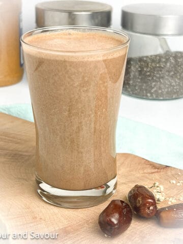 A glass of chocolate peanut butter smoothie with jars of ingredients in the background.